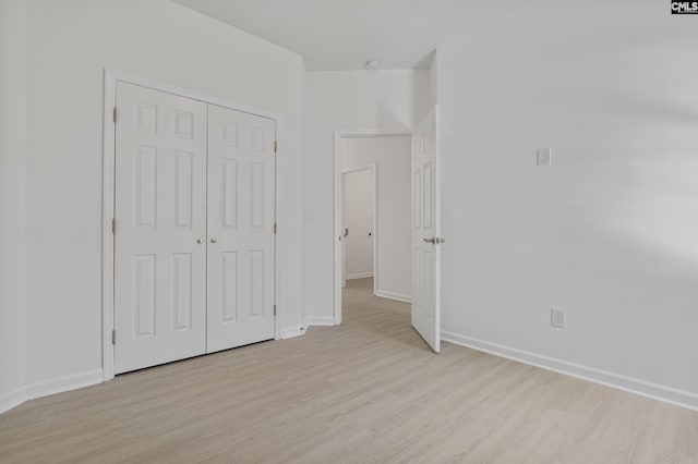 unfurnished bedroom featuring light wood-style floors, baseboards, and a closet