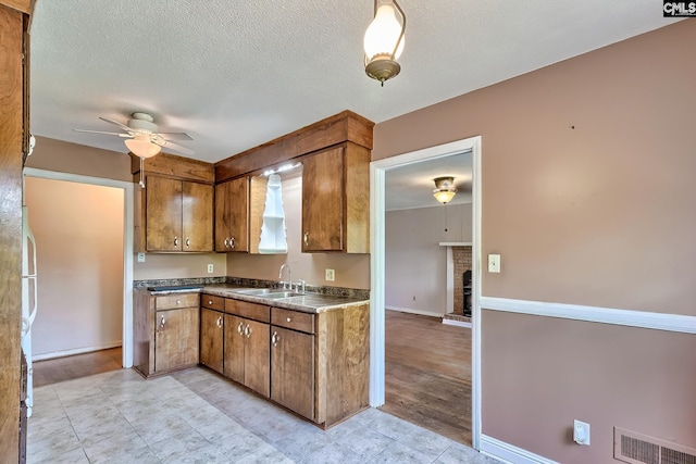 kitchen featuring brown cabinetry, a ceiling fan, visible vents, a fireplace, and a sink