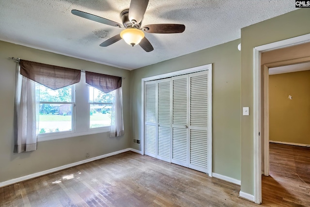 unfurnished bedroom featuring a textured ceiling, baseboards, a closet, and wood finished floors