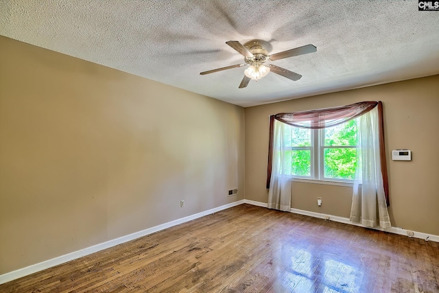 empty room featuring ceiling fan, a textured ceiling, visible vents, wood finished floors, and baseboards