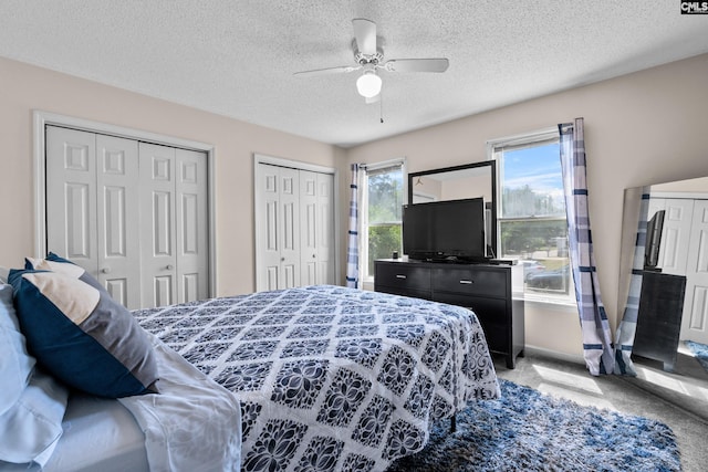 bedroom featuring carpet flooring, a textured ceiling, ceiling fan, and two closets