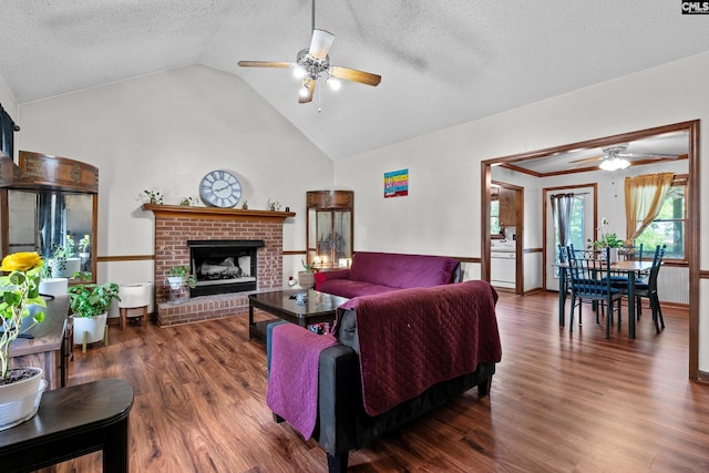 living room with a brick fireplace, wood finished floors, high vaulted ceiling, a textured ceiling, and a ceiling fan