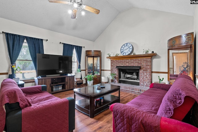 living room featuring wood finished floors, a fireplace, ceiling fan, high vaulted ceiling, and a textured ceiling