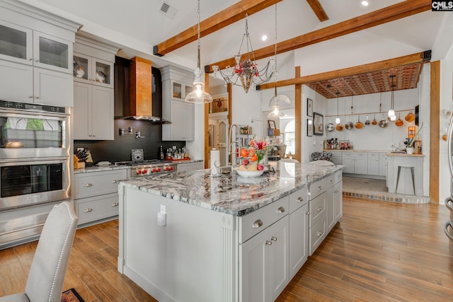 kitchen featuring visible vents, beam ceiling, double oven, light wood-type flooring, and wall chimney exhaust hood
