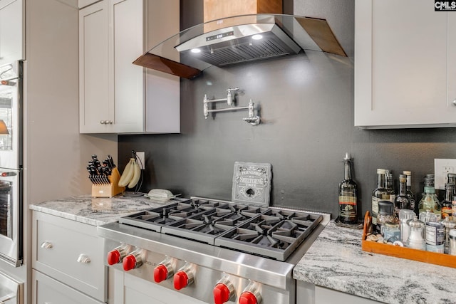 kitchen featuring extractor fan, oven, stovetop, white cabinets, and light stone countertops