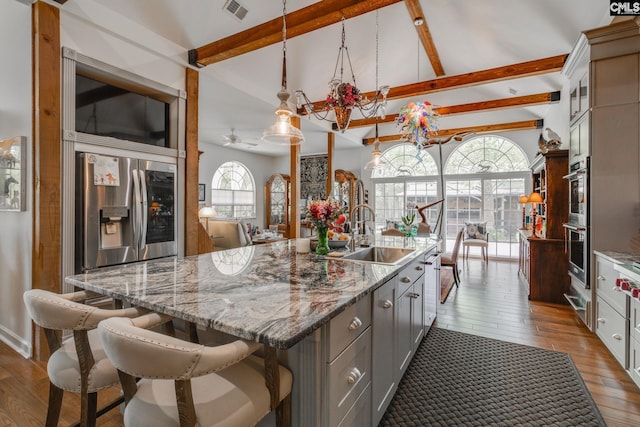 kitchen featuring a sink, lofted ceiling with beams, a kitchen island with sink, dark wood-type flooring, and appliances with stainless steel finishes