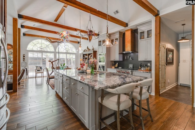 kitchen with gray cabinetry, beamed ceiling, visible vents, and wall chimney exhaust hood