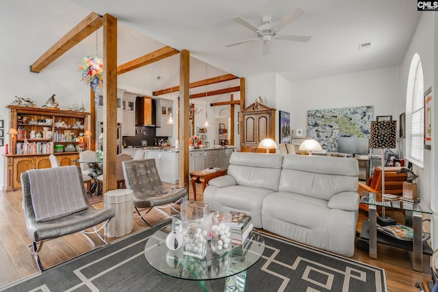 living area with visible vents, light wood-style flooring, ceiling fan, and vaulted ceiling with beams