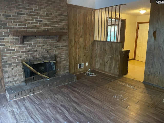 unfurnished living room featuring wood walls, wood finished floors, a fireplace, and visible vents