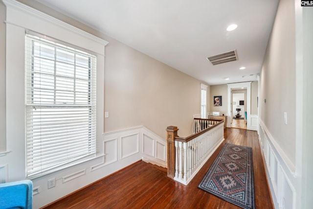corridor featuring visible vents, a healthy amount of sunlight, a wainscoted wall, dark wood finished floors, and an upstairs landing