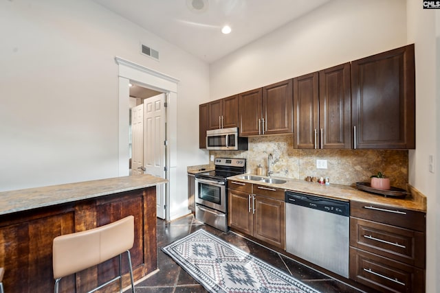 kitchen with stainless steel appliances, dark brown cabinetry, decorative backsplash, and a sink