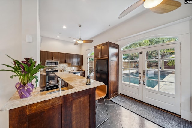 kitchen featuring a peninsula, ceiling fan, a sink, appliances with stainless steel finishes, and backsplash