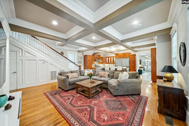 living room featuring light wood-style floors, ornamental molding, beamed ceiling, and stairs