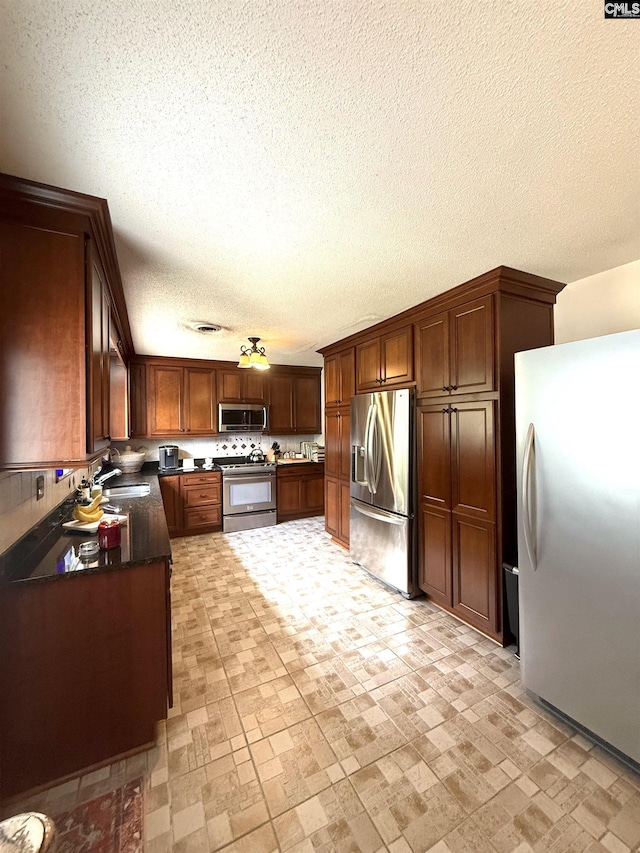 kitchen featuring a sink, dark countertops, a textured ceiling, visible vents, and appliances with stainless steel finishes