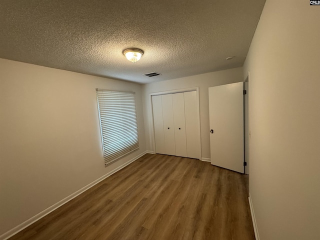 unfurnished bedroom with baseboards, visible vents, a textured ceiling, and wood finished floors