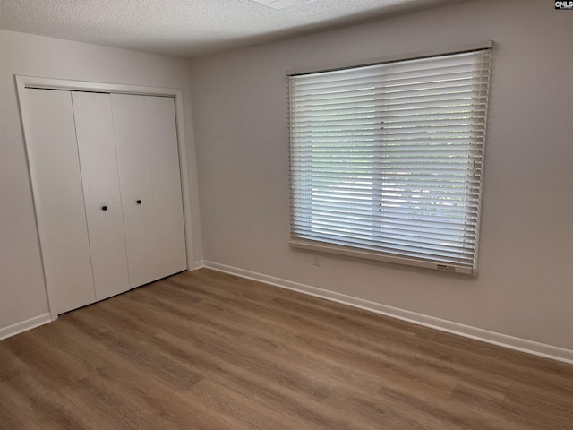 unfurnished bedroom with baseboards, a closet, a textured ceiling, and wood finished floors