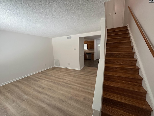 staircase with visible vents, a textured ceiling, and wood finished floors