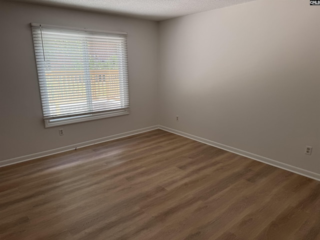 spare room featuring baseboards, a textured ceiling, and dark wood-type flooring