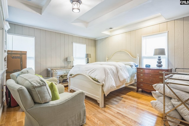 bedroom featuring multiple windows, light wood-type flooring, visible vents, and wood walls