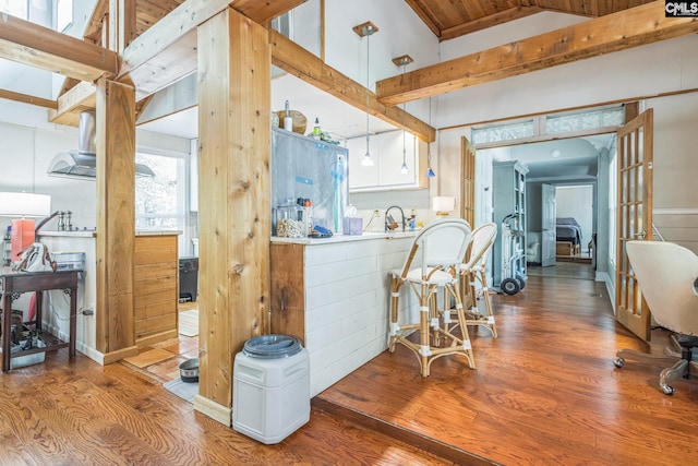 kitchen with a sink, wood finished floors, white cabinetry, hanging light fixtures, and vaulted ceiling with beams