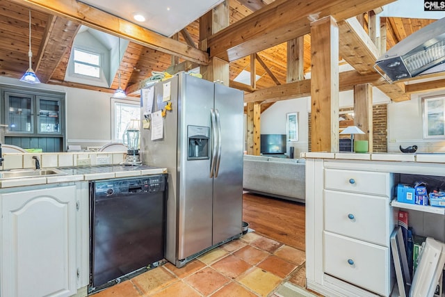 kitchen featuring tile countertops, lofted ceiling with skylight, black dishwasher, a sink, and stainless steel fridge