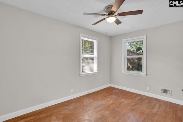 empty room with a ceiling fan, a wealth of natural light, visible vents, and wood finished floors