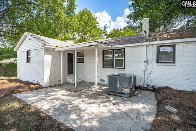 rear view of property featuring brick siding, crawl space, a patio, a chimney, and central AC unit