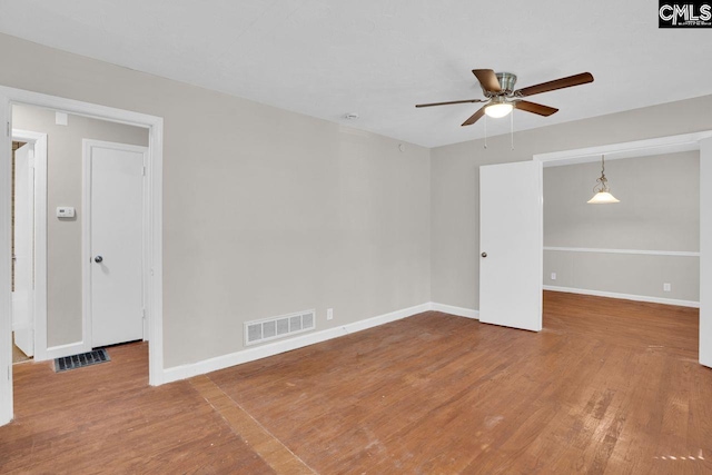 empty room featuring baseboards, visible vents, wood finished floors, and a ceiling fan