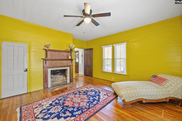 living area featuring ceiling fan, wood walls, hardwood / wood-style floors, and a fireplace with flush hearth