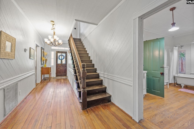 foyer entrance with a notable chandelier, ornamental molding, light wood finished floors, stairs, and wood walls