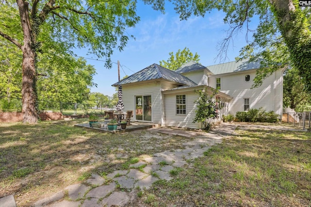back of house featuring a lawn, a patio area, metal roof, and fence