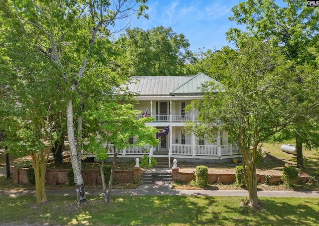 view of front of home featuring a balcony, a standing seam roof, metal roof, covered porch, and a front lawn