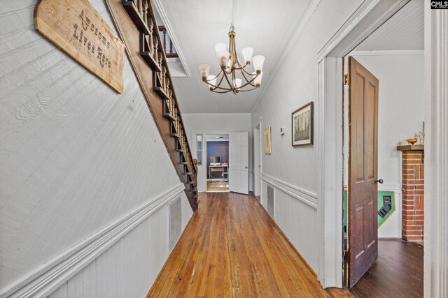 hall featuring stairs, an inviting chandelier, crown molding, and wood finished floors
