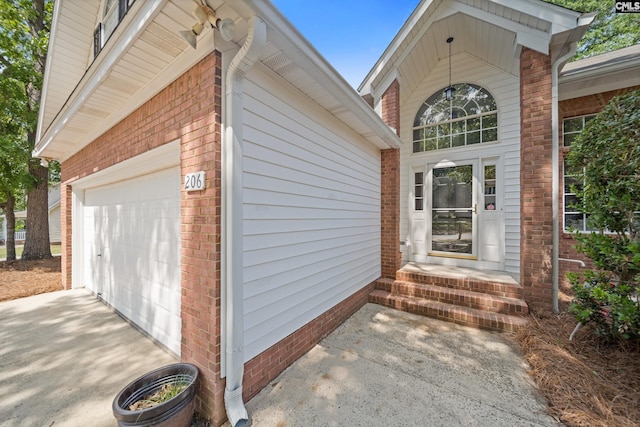doorway to property featuring driveway, brick siding, and an attached garage