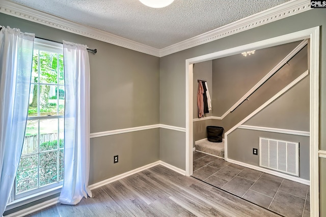 unfurnished room with wood finished floors, a textured ceiling, visible vents, crown molding, and baseboards