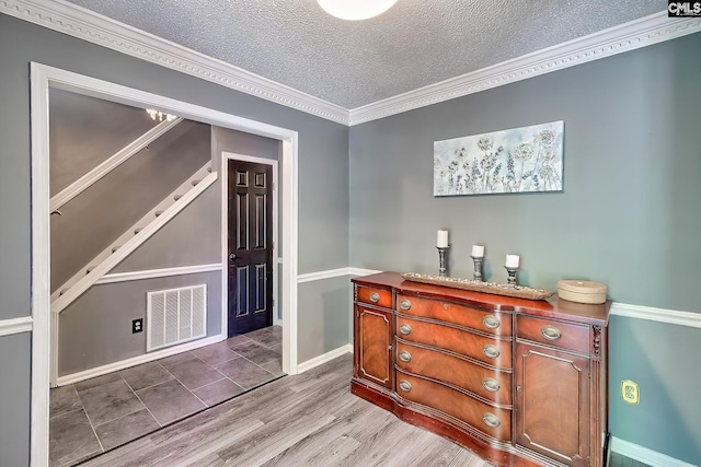 bar featuring wood finished floors, crown molding, a textured ceiling, visible vents, and baseboards