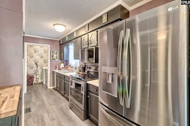 kitchen with a sink, crown molding, a textured ceiling, and appliances with stainless steel finishes