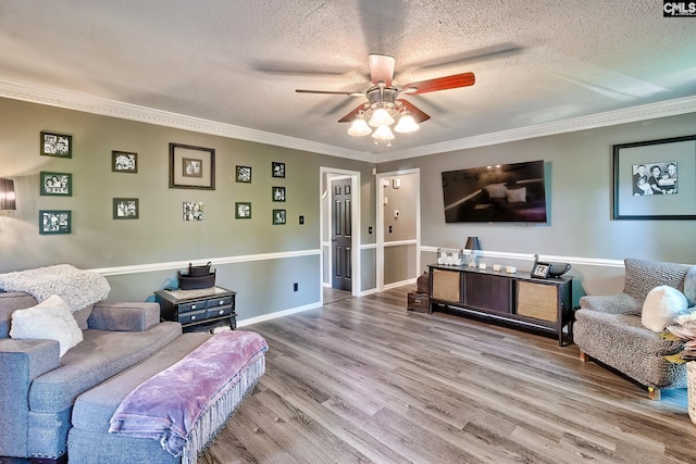 living room with a ceiling fan, ornamental molding, a textured ceiling, and wood finished floors