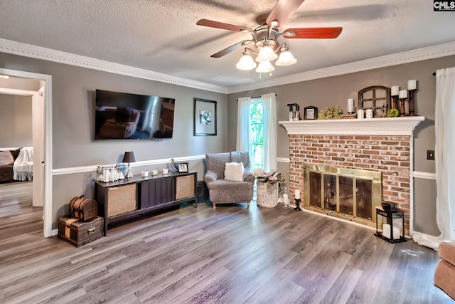 living area with crown molding, wood finished floors, a ceiling fan, and a fireplace