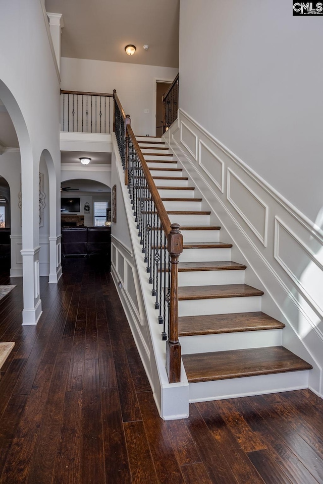 staircase with a high ceiling, a wainscoted wall, a decorative wall, arched walkways, and hardwood / wood-style flooring