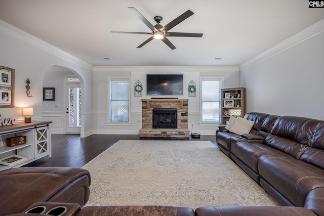 living area featuring dark wood-style floors, ornamental molding, arched walkways, and a ceiling fan