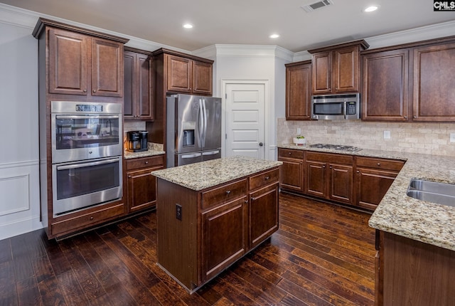 kitchen featuring appliances with stainless steel finishes, light stone counters, dark wood-style flooring, and ornamental molding