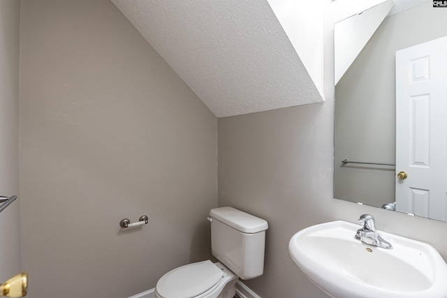 half bath with toilet, a sink, a textured ceiling, baseboards, and vaulted ceiling