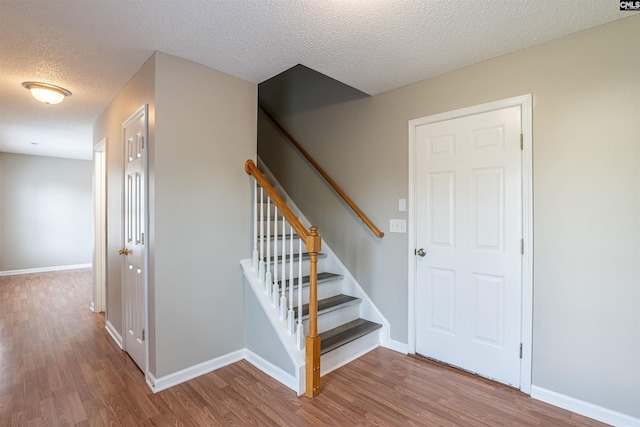 stairs with a textured ceiling, baseboards, and wood finished floors