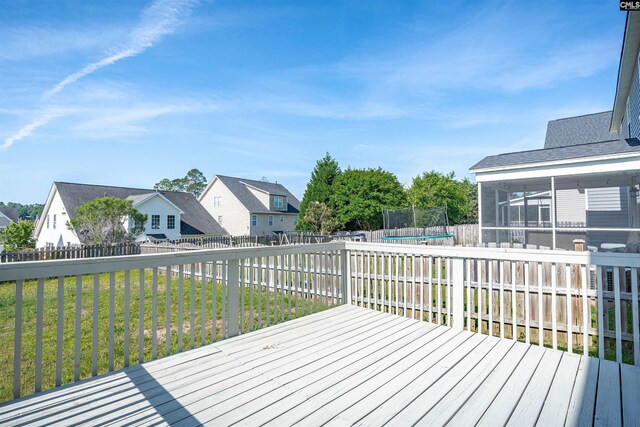 wooden deck with a trampoline, a residential view, a fenced backyard, a lawn, and a sunroom