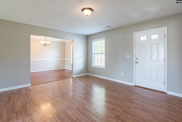 entryway featuring wood finished floors, a textured ceiling, visible vents, an inviting chandelier, and baseboards