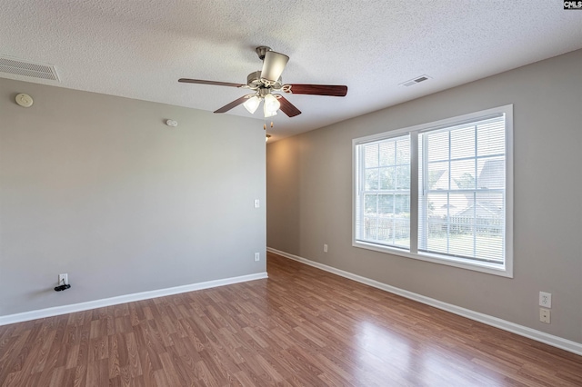 unfurnished room with a textured ceiling, baseboards, ceiling fan, visible vents, and wood finished floors