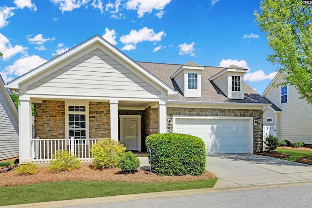 view of front of home with driveway, covered porch, a garage, stone siding, and roof with shingles