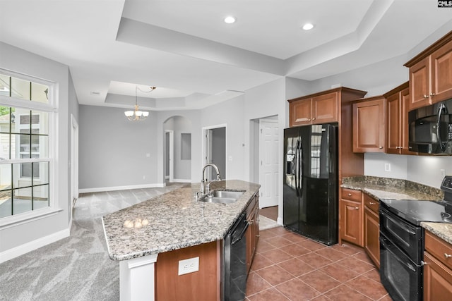 kitchen featuring brown cabinetry, a sink, arched walkways, a raised ceiling, and black appliances