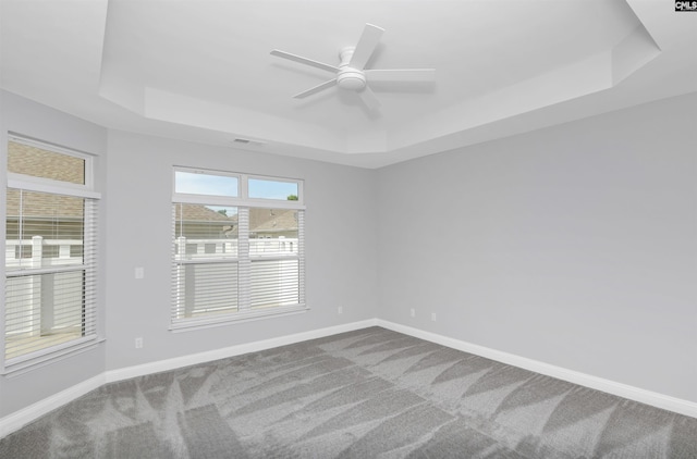 carpeted spare room featuring a ceiling fan, visible vents, baseboards, and a raised ceiling